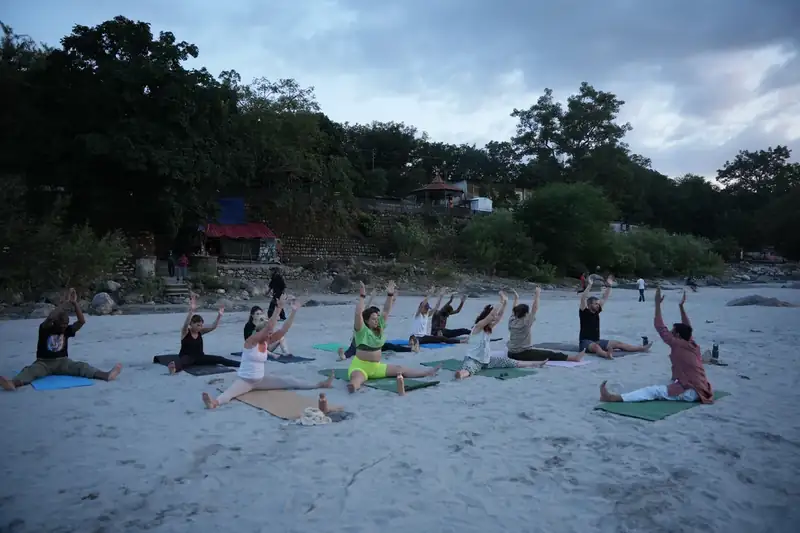 Ashtanga yoga class practising with arms raised at sunrise beside the Ganges in Rishikesh